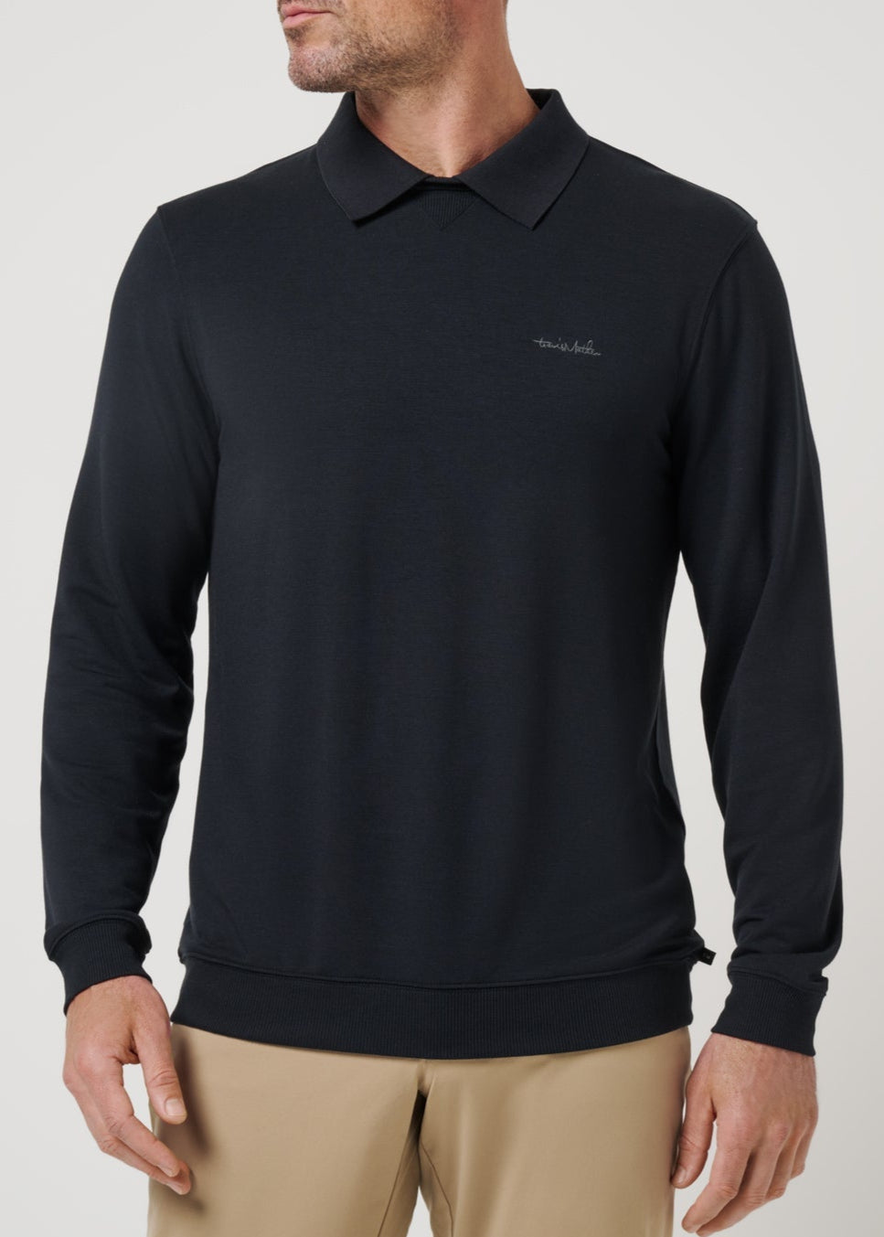 Man wearing a black long-sleeve polo shirt with a logo on a light gray background