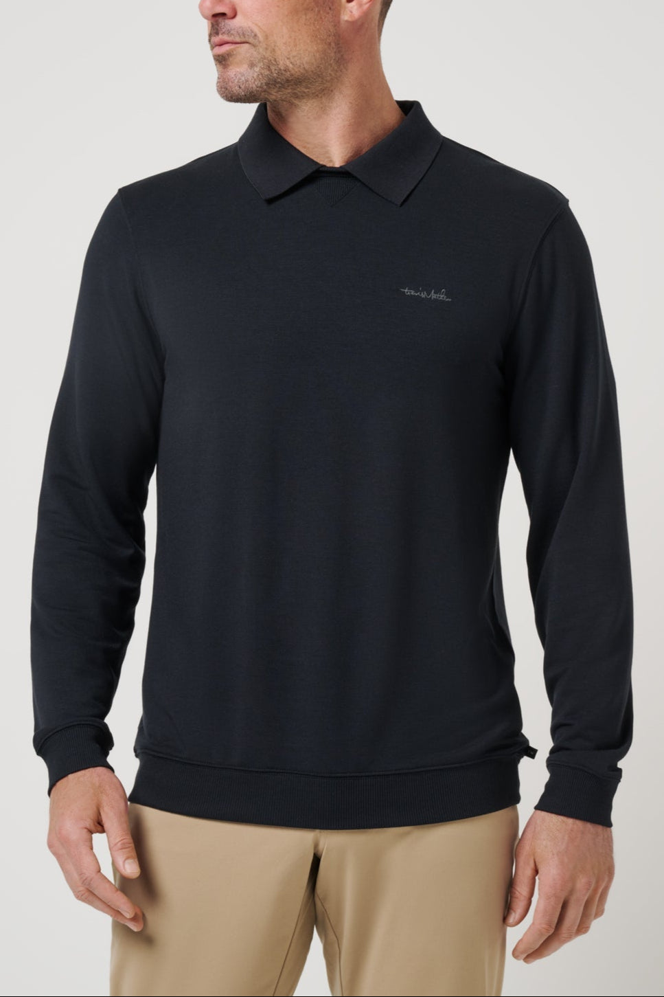 Man wearing a black long-sleeve polo shirt with a logo on a light gray background