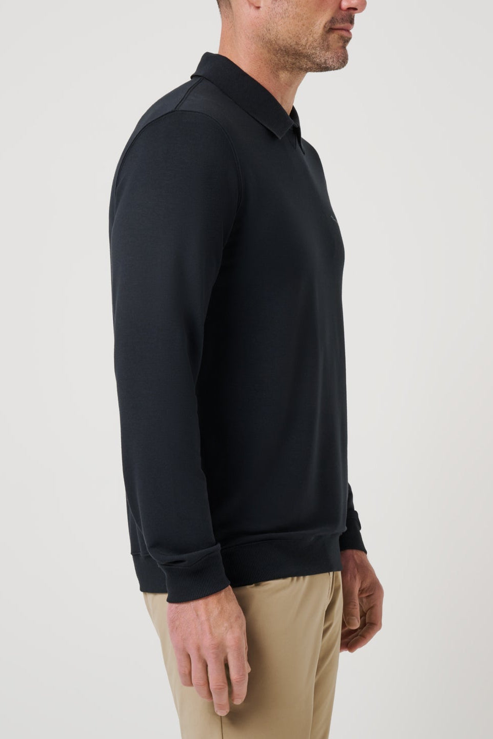 Man wearing a black long-sleeve shirt and beige pants on a white background