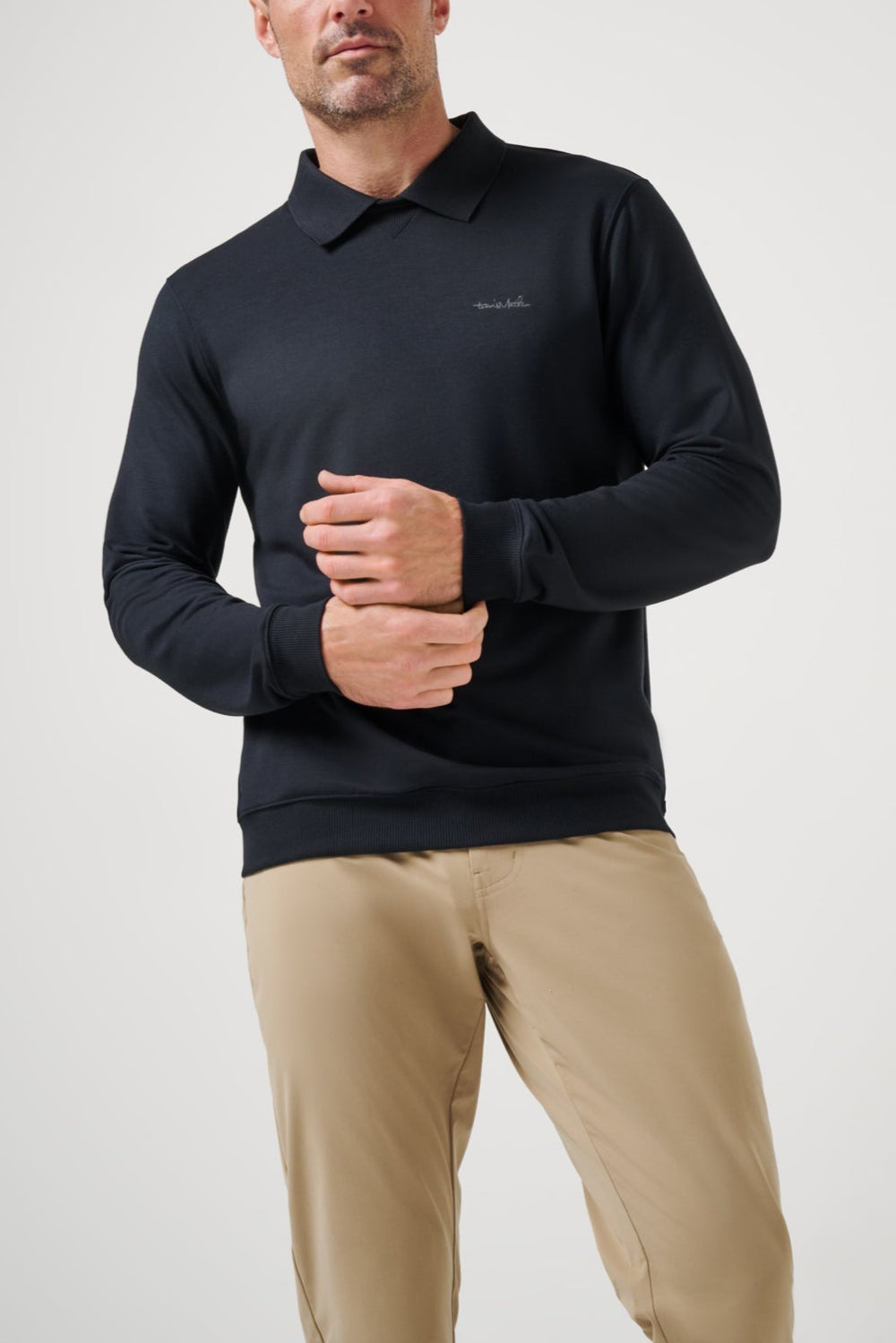 Man wearing a black long-sleeve polo shirt and beige pants on a light gray background