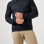 Man wearing a black long-sleeve polo shirt and beige pants on a light gray background