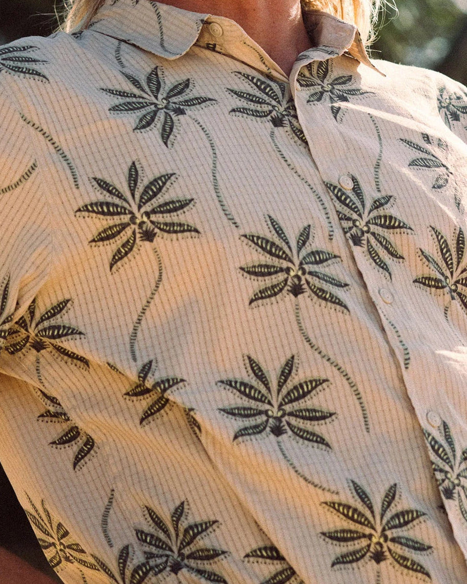 Man wearing a patterned shirt and cap with palm trees in the background