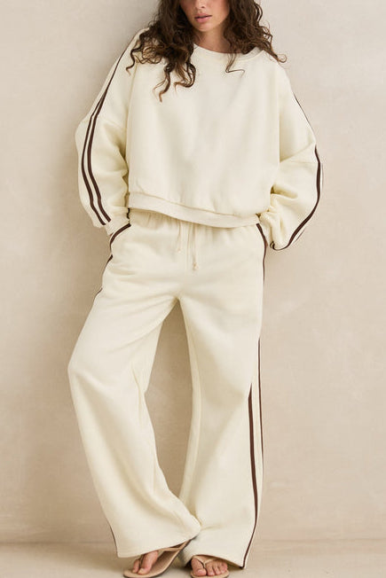 Woman wearing a cream-colored outfit with black trim against a beige background