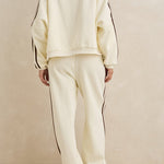 Person wearing a cream-colored tracksuit with black stripes on a beige background