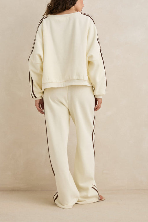 Person wearing a cream-colored tracksuit with black stripes on a beige background
