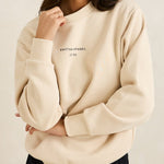 Woman wearing a beige sweatshirt with text on it against a plain background