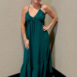 Woman in a teal dress standing against a beige wall.