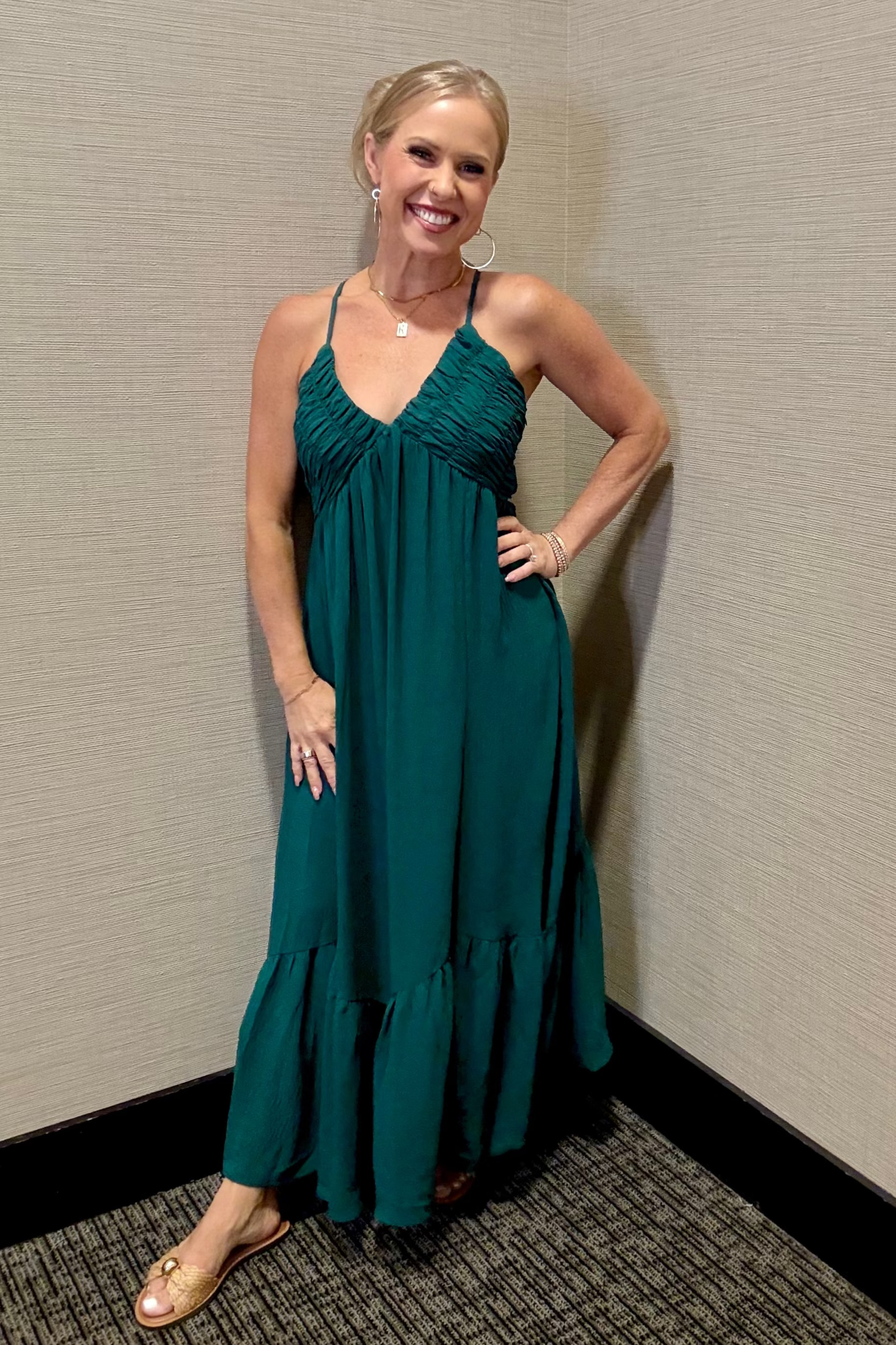 Woman in a teal dress standing against a beige wall.