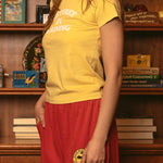Woman wearing yellow Duvin In Training baby tee with red skirt in lifestyle setting