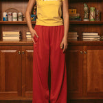Woman wearing yellow baby tee with red pants standing in front of wooden bookshelf