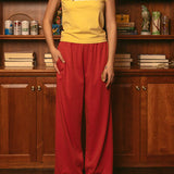 Woman wearing yellow baby tee with red pants standing in front of wooden bookshelf