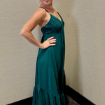 Woman in a teal dress posing against a beige wall.