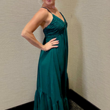 Woman in a teal dress posing against a beige wall.