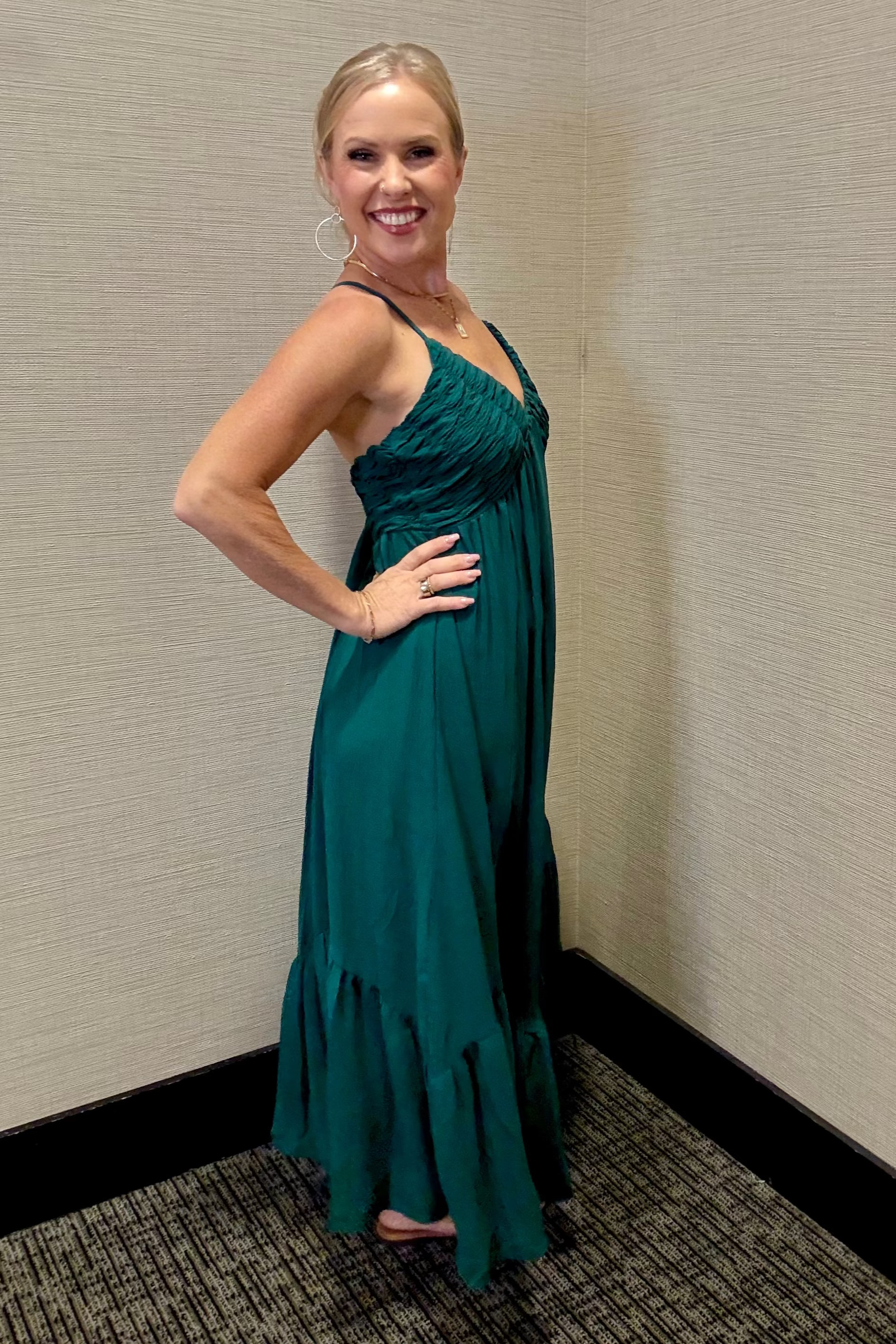 Woman in a teal dress posing against a beige wall.