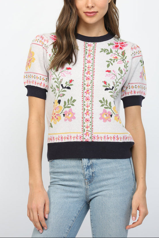 Woman wearing a floral embroidered sweater and jeans on a white background