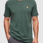 Man wearing a green t-shirt with a small logo on a gray background