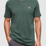 Man wearing a green t-shirt with a small logo on a gray background
