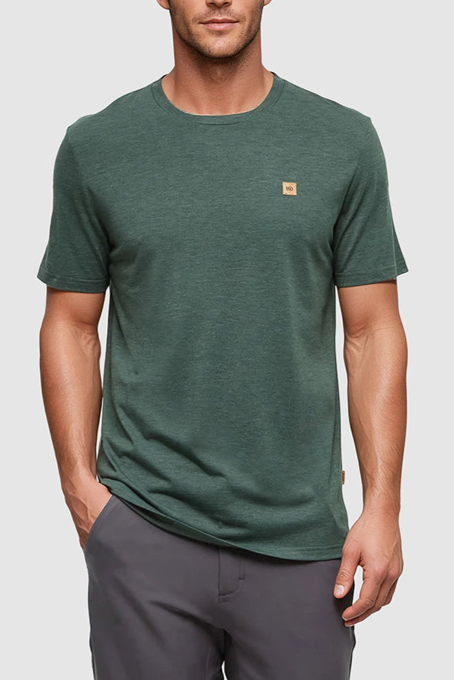 Man wearing a green t-shirt with a small logo on a gray background