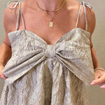 Woman wearing a silver dress with a bow detail against a neutral background