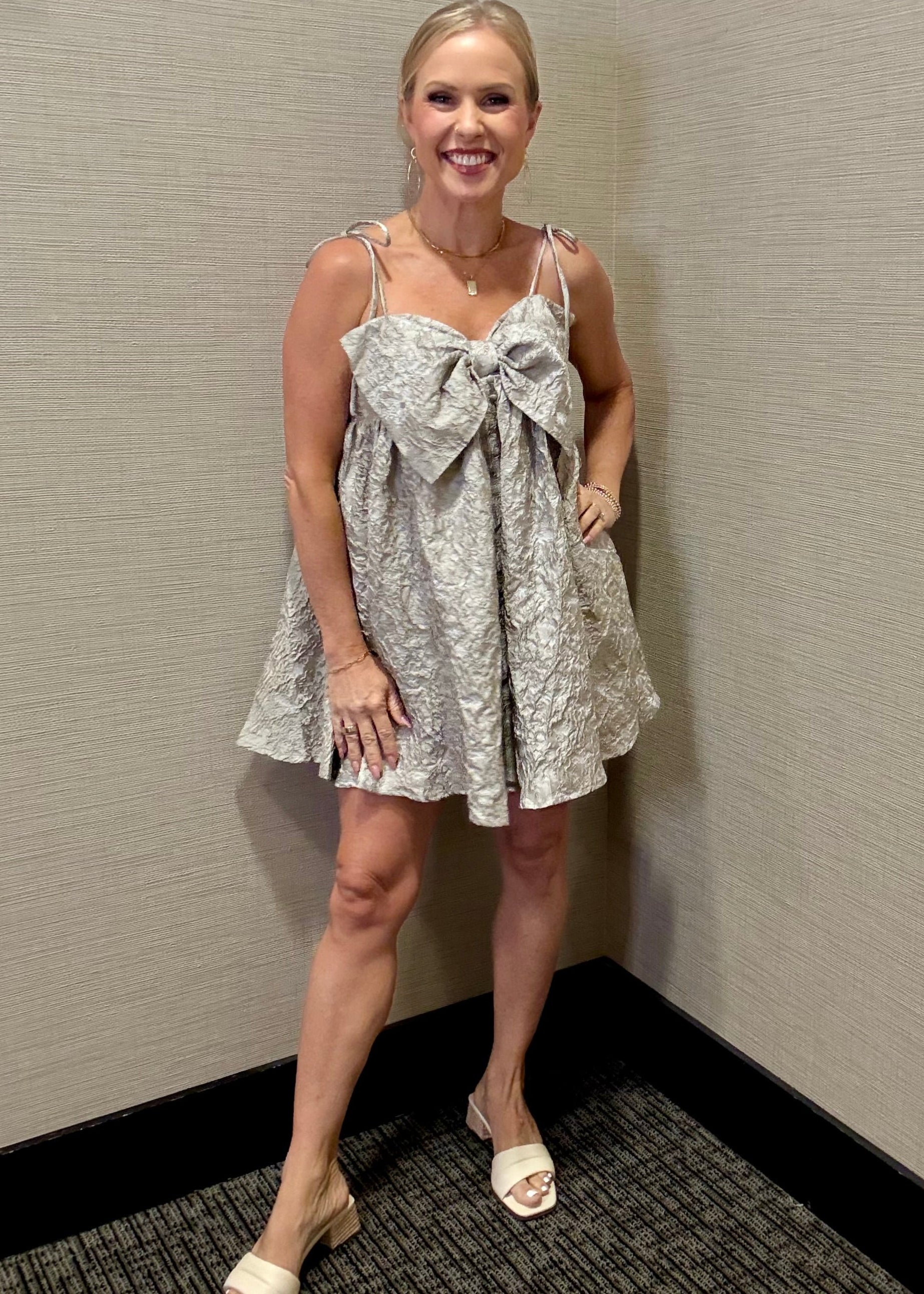 Woman in a patterned dress standing against a plain wall.