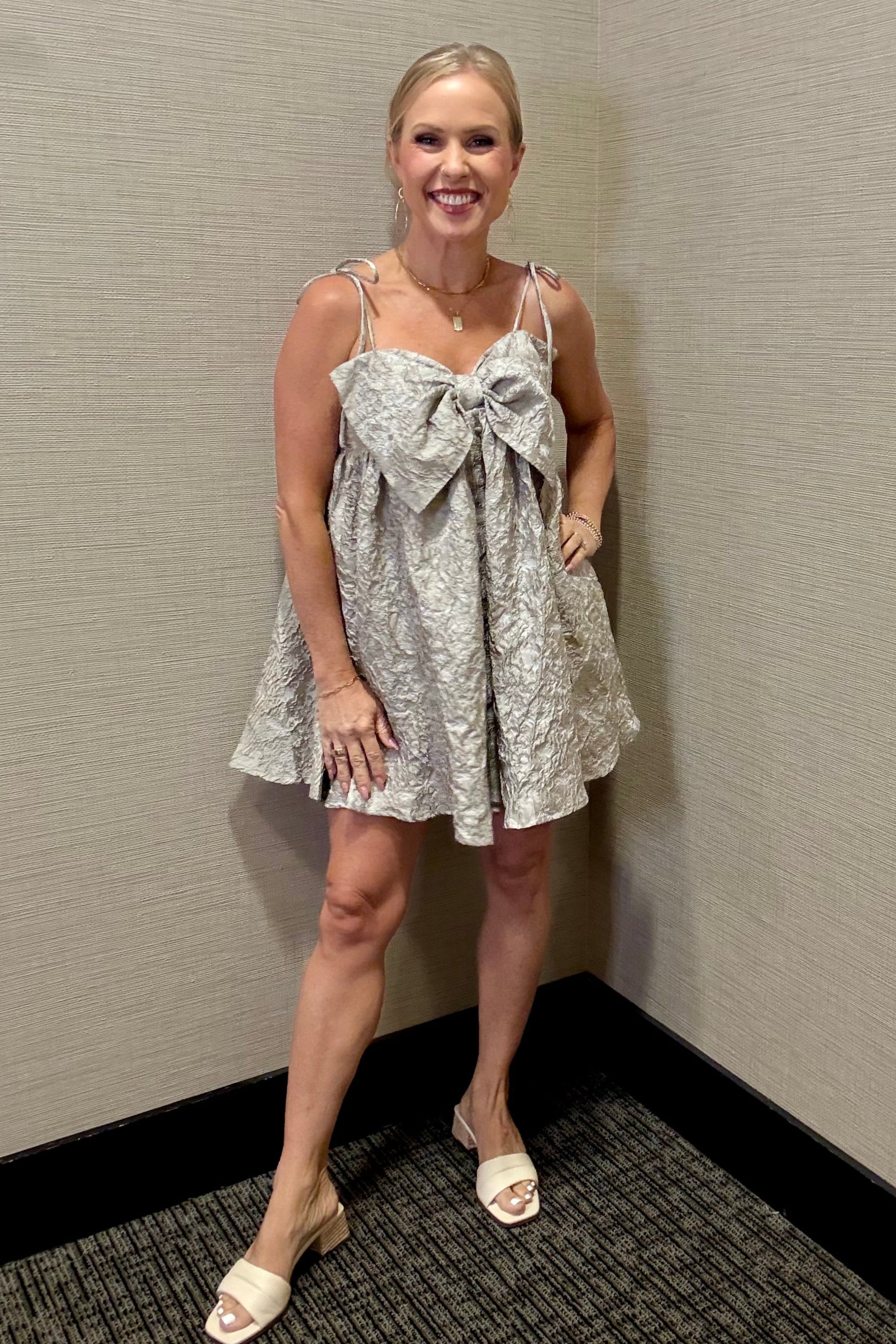 Woman in a patterned dress standing against a plain wall.