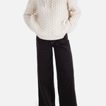 Person wearing a textured white sweater and black pants on a white background