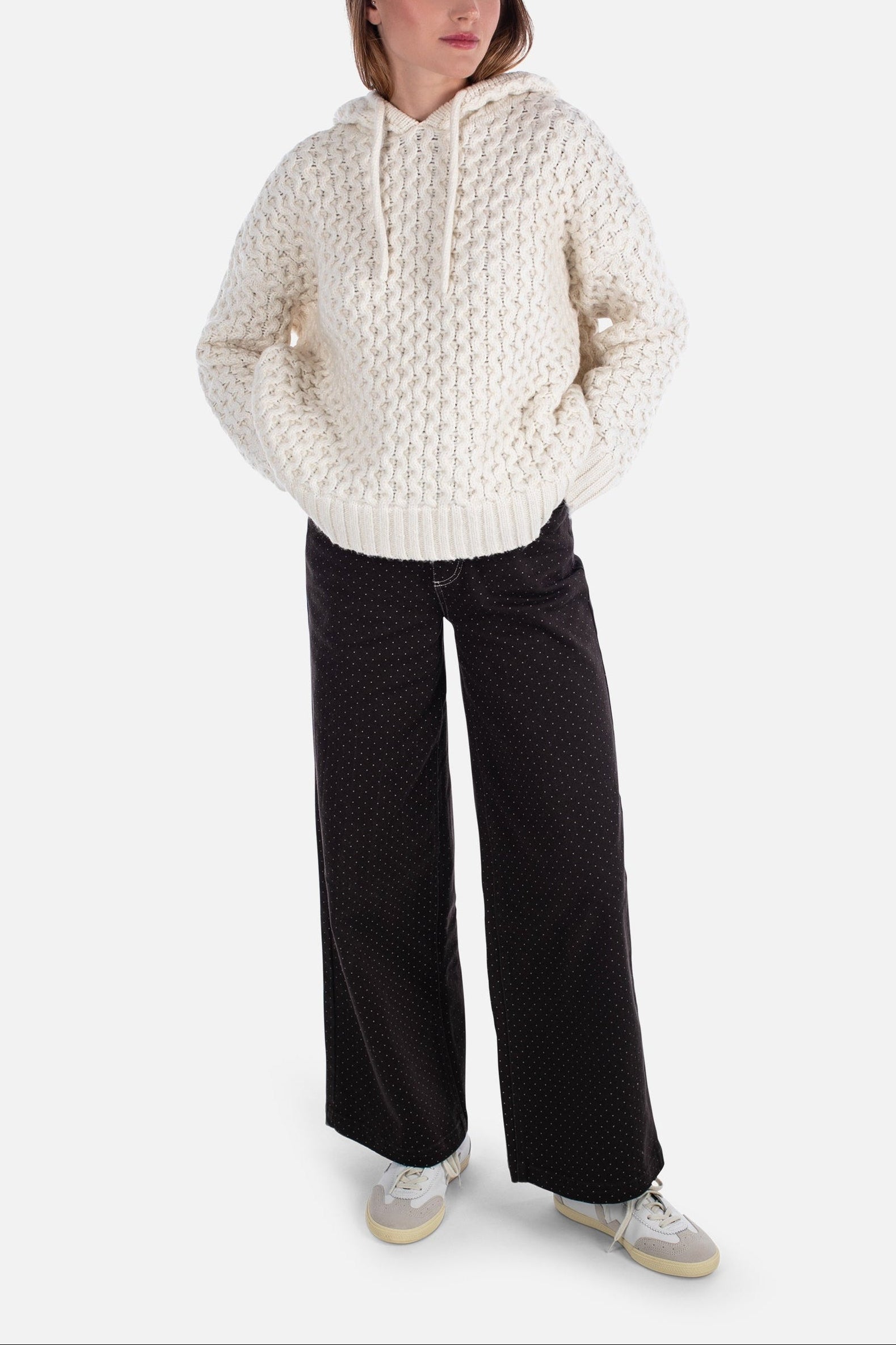 Person wearing a textured white sweater and black pants on a white background