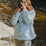 Person taking a photo by a body of water wearing a denim jacket.