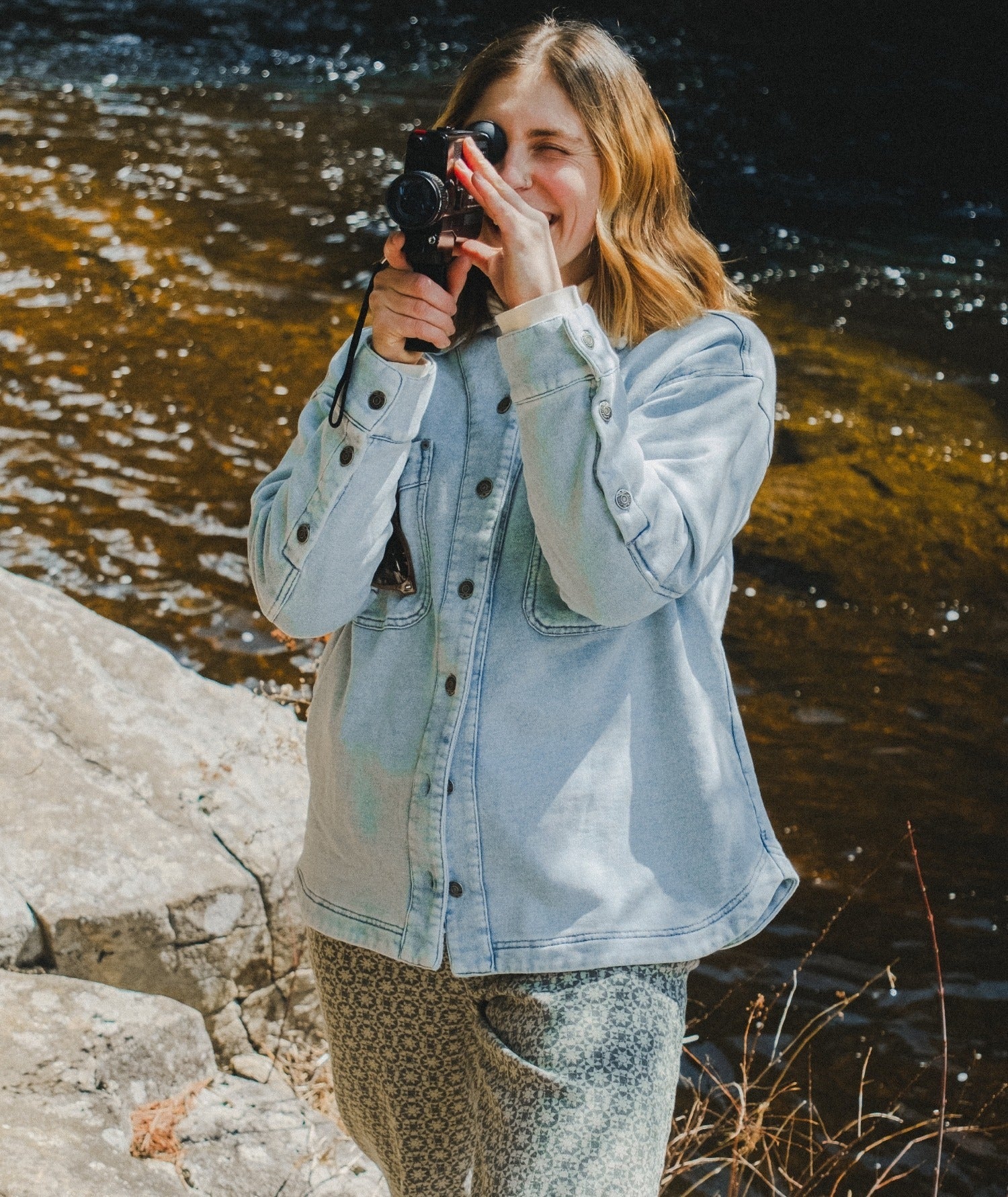 Person taking a photo by a body of water wearing a denim jacket.