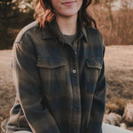 Woman sitting outdoors in a field wearing a green plaid shirt.