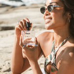 Woman holding Kuya cologne on a tropical beach