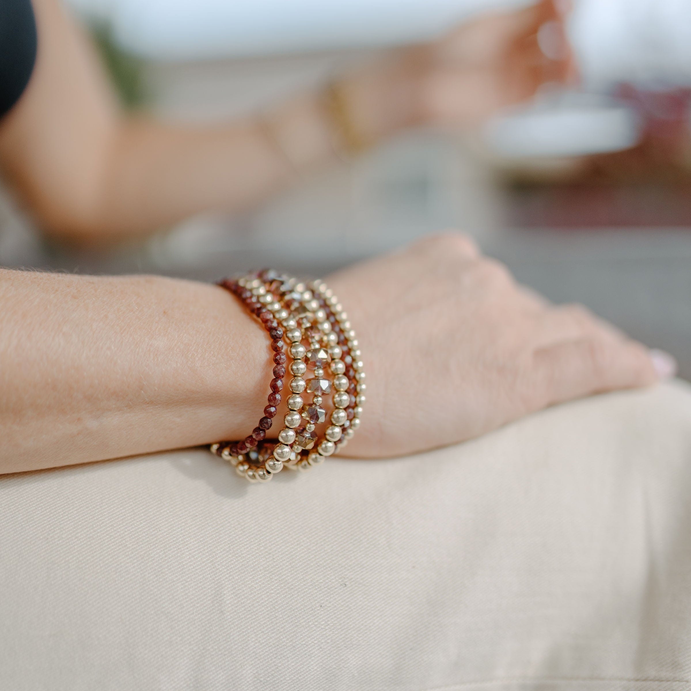 Close-up of a person's wrist wearing multiple beaded bracelets with a blurred background.