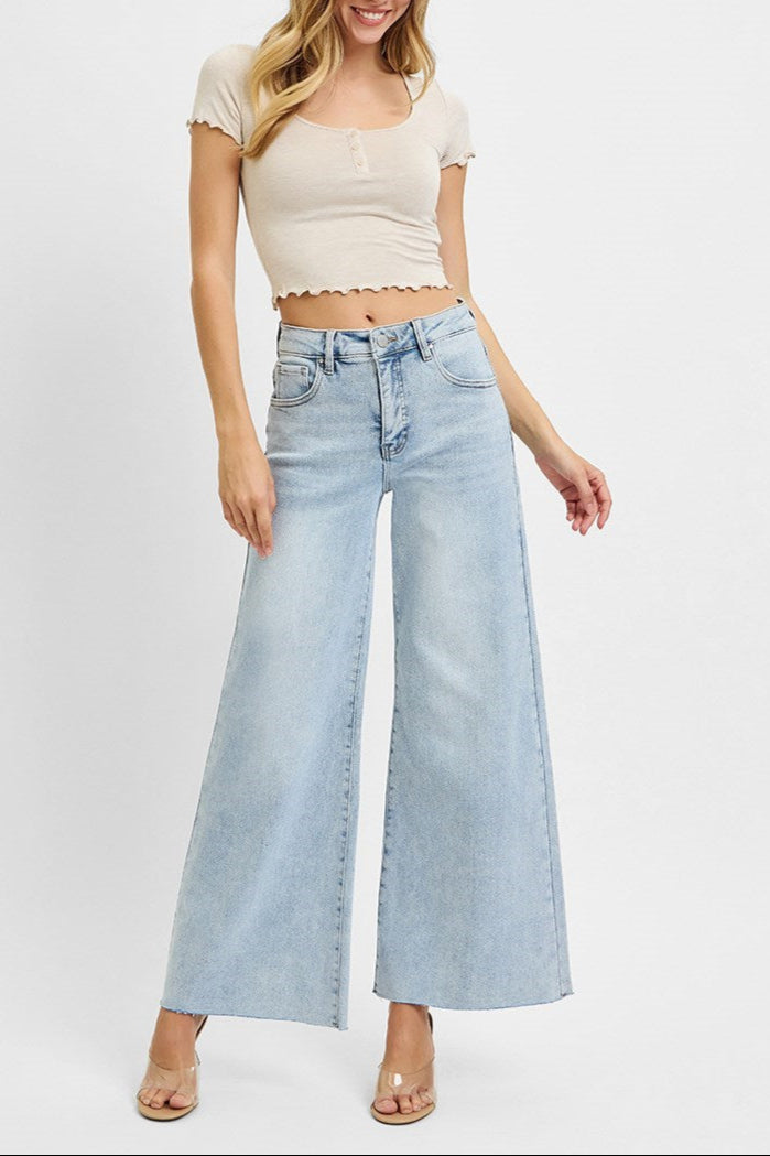 Woman wearing a beige crop top and light blue wide-leg jeans on a white background