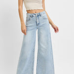 Woman wearing a beige crop top and light blue wide-leg jeans on a white background