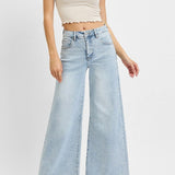 Woman wearing a beige crop top and light blue wide-leg jeans on a white background