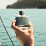Hand holding Guy Fox Riviera cologne bottle above the water on a boat
