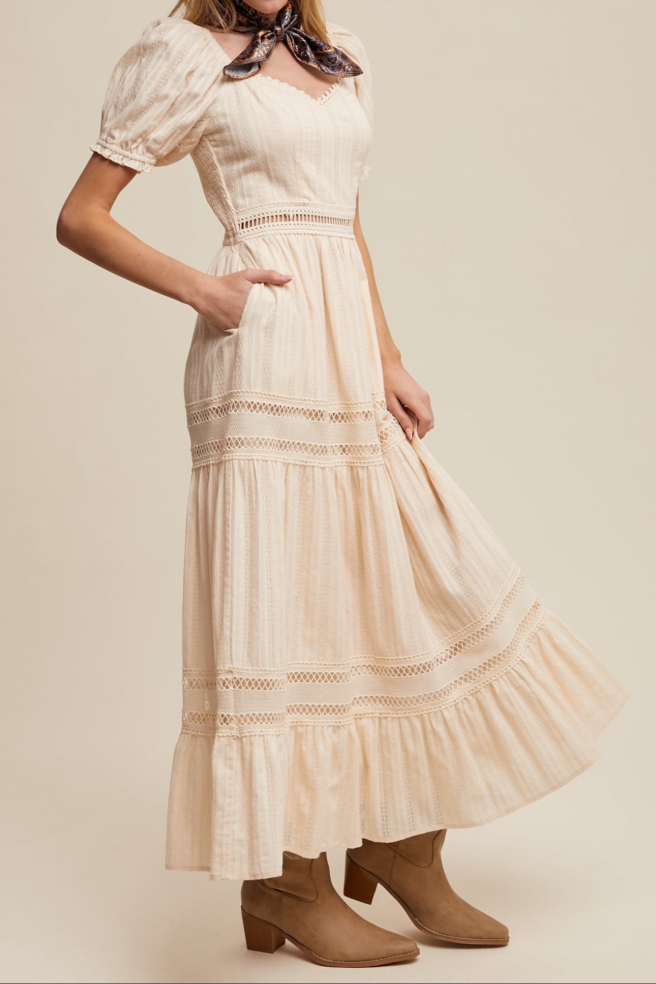 Woman wearing a beige lace dress with brown boots on a plain background