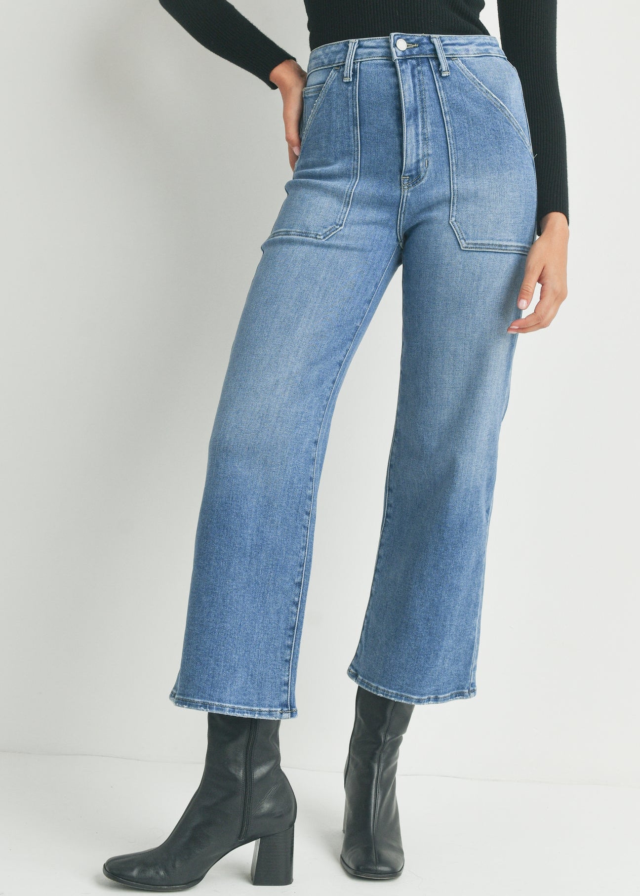 Person wearing high-waisted blue jeans and black boots on a plain background