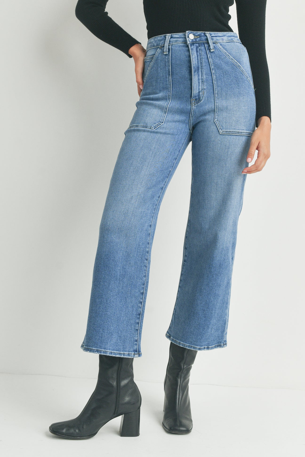 Person wearing high-waisted blue jeans and black boots on a plain background