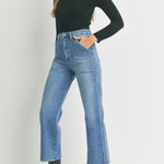 Woman wearing a black turtleneck, blue jeans, and black boots on a white background