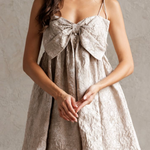Woman wearing a beige lace dress with a large bow detail on a plain background