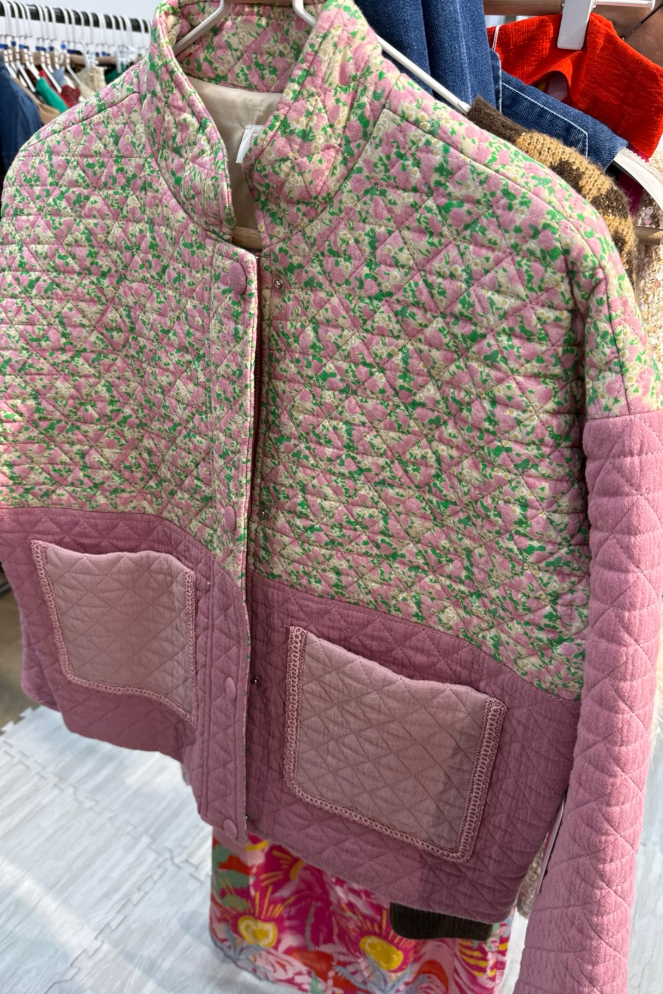 Pink quilted jacket with floral pattern on a hanger