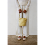 Butter yellow Vancouver bucket bag carried with a white outfit