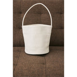 Ivory woven Vancouver bucket bag resting on a brown couch