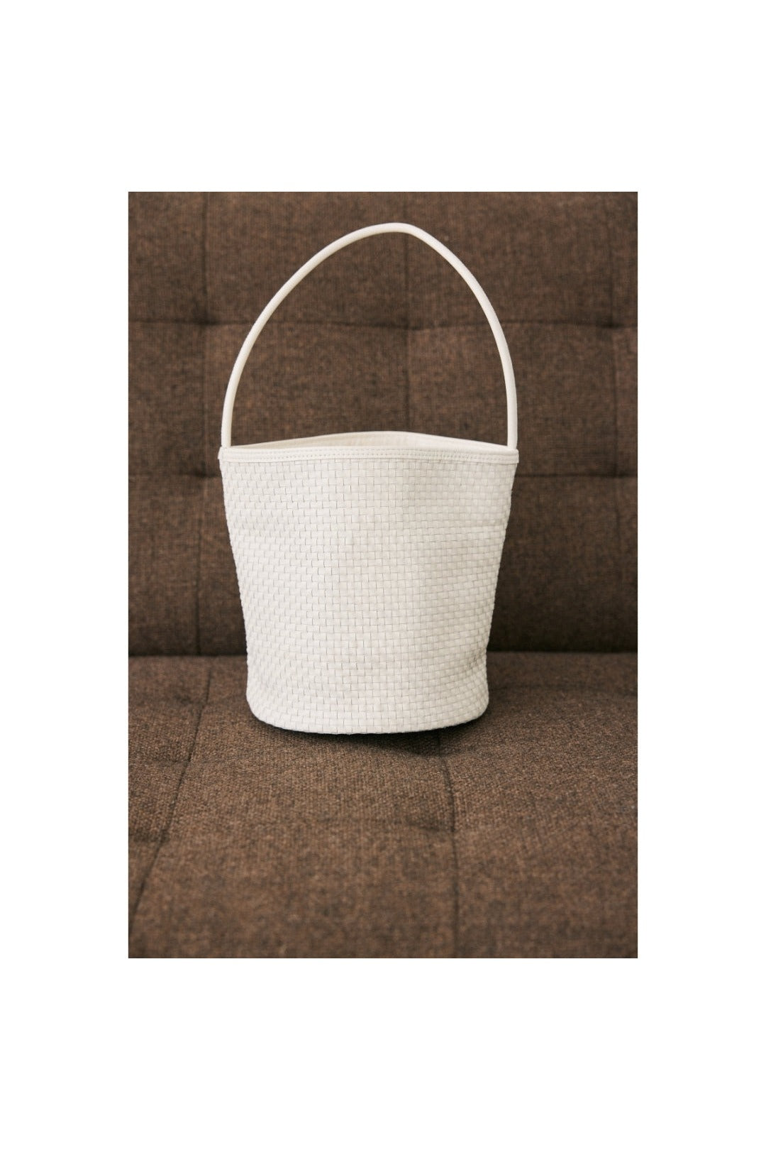 Ivory woven Vancouver bucket bag resting on a brown couch