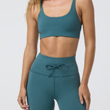 Woman wearing a teal sports bra and leggings on a white background