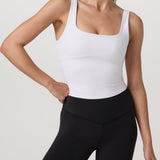 Woman wearing a white tank top and black leggings on a plain background