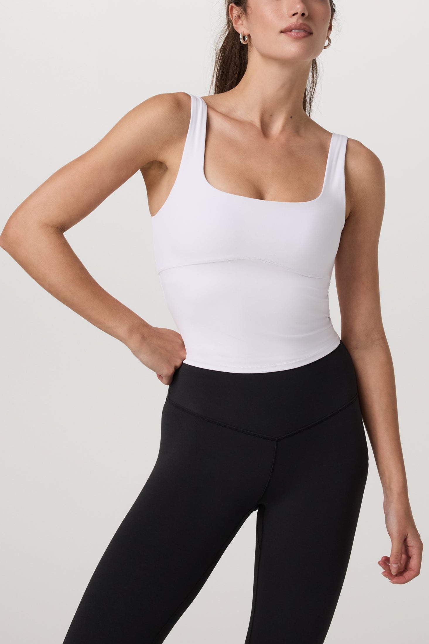 Woman wearing a white tank top and black leggings on a plain background