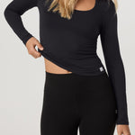 Woman wearing a black long-sleeve top and leggings on a light gray background