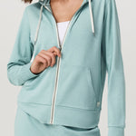 Woman wearing a light blue hoodie and pants on a plain background